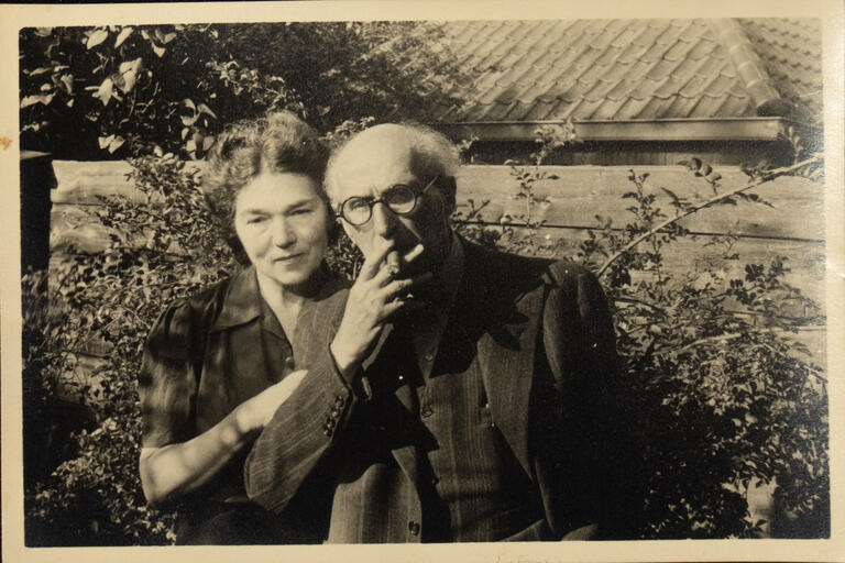 Sinzheimer und seine Frau. Sinzheimer hat eine Zigarre im Mund. Beide stehen vor einer Hecke. Im Hintergrund ist ein Dach zu sehen.