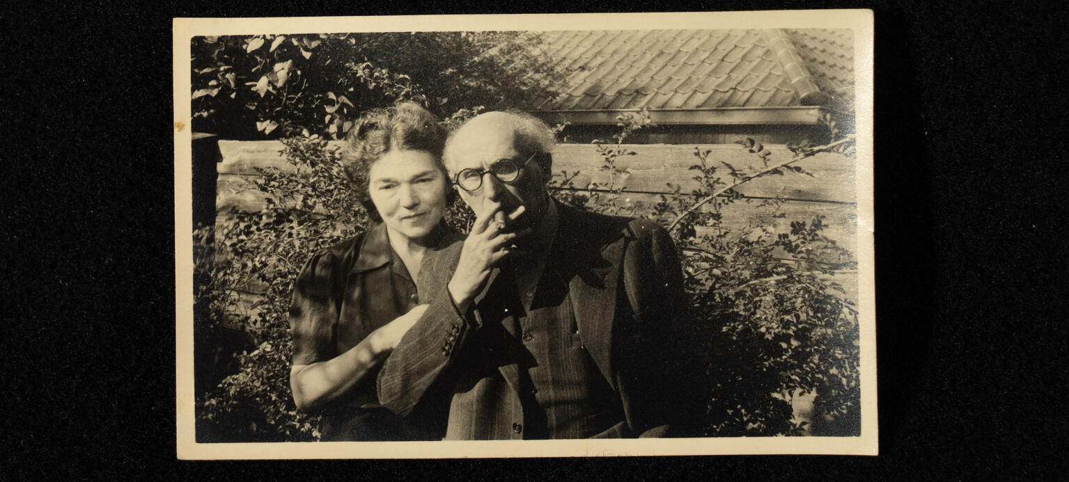 Sinzheimer und seine Frau vor einer Hecke und im Hintergrund ein Dach. Sinzheimer raucht eine Zigarre. 